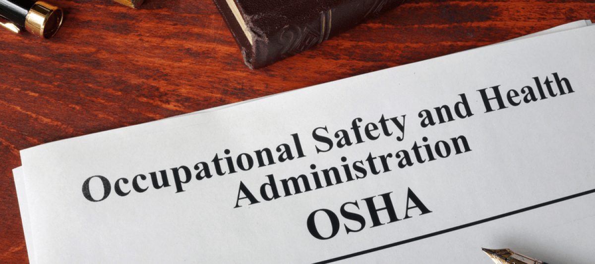 Occupational Safety and Health Administration OSHA papers, a book, and a pen on wooden table