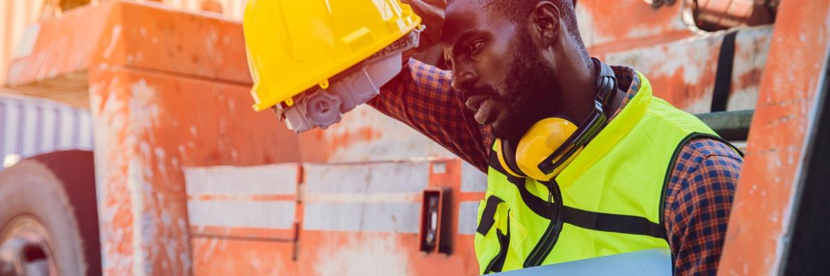 man in hard hat holding a laptop in the heat, wiping brow